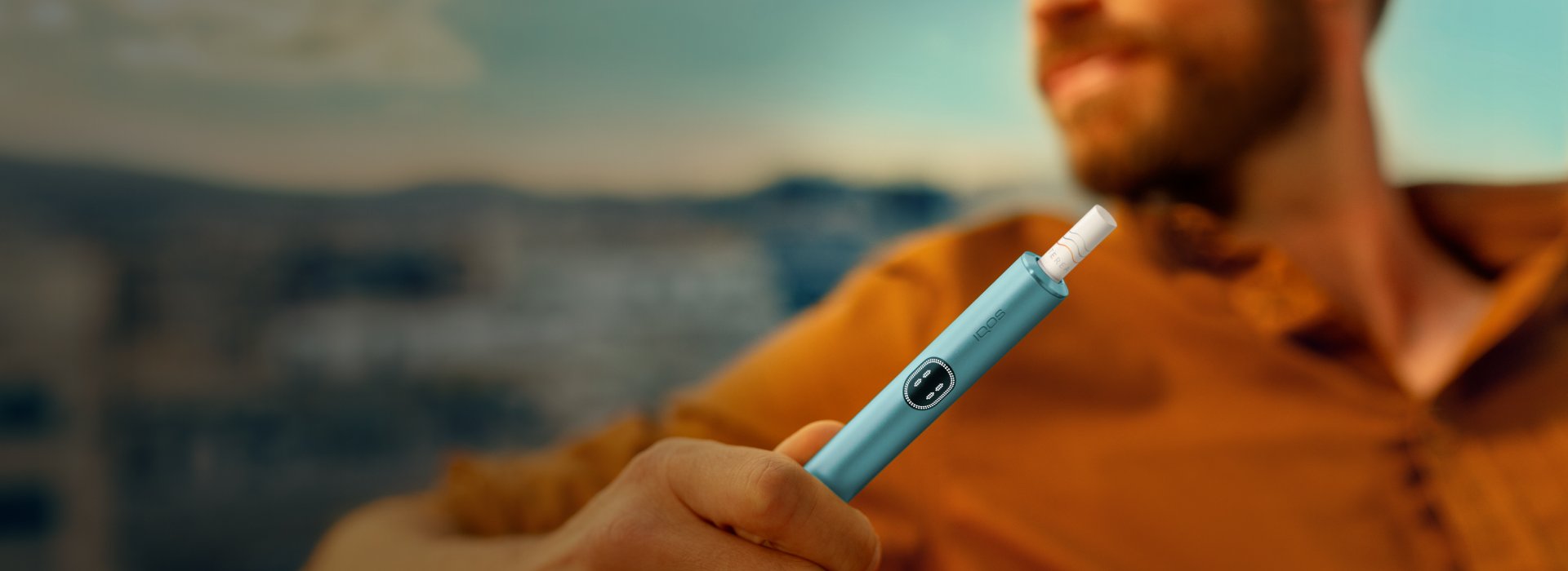 Man holding an IQOS ILUMA i holder outdoors, showcasing a modern smoke-free lifestyle product.